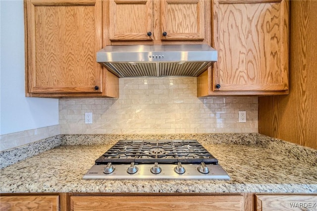 kitchen with stainless steel gas cooktop, wall chimney exhaust hood, backsplash, and light stone countertops