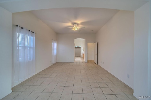 empty room featuring arched walkways, light tile patterned flooring, and a ceiling fan