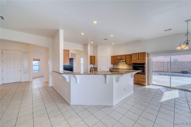 kitchen featuring light tile patterned floors, stone countertops, a breakfast bar area, brown cabinets, and black appliances