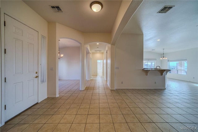 foyer entrance with light tile patterned floors, arched walkways, visible vents, and a notable chandelier