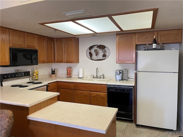 kitchen with brown cabinets, light countertops, a sink, a peninsula, and black appliances