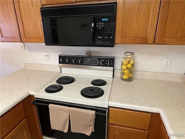 kitchen featuring black microwave, light countertops, electric range oven, brown cabinetry, and mail area