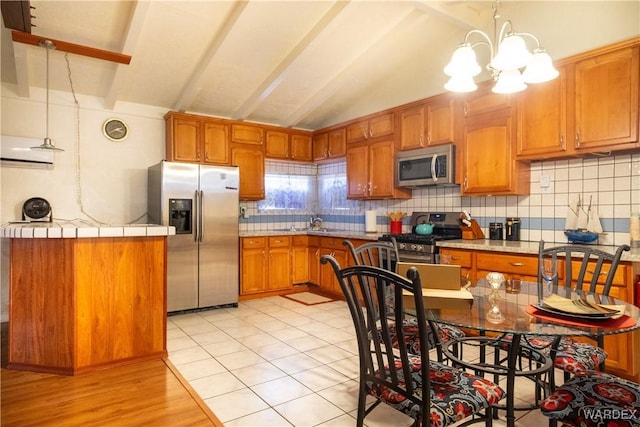 kitchen with tasteful backsplash, appliances with stainless steel finishes, brown cabinets, hanging light fixtures, and vaulted ceiling with beams