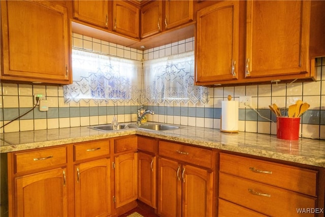 kitchen with backsplash, light stone counters, brown cabinetry, and a sink