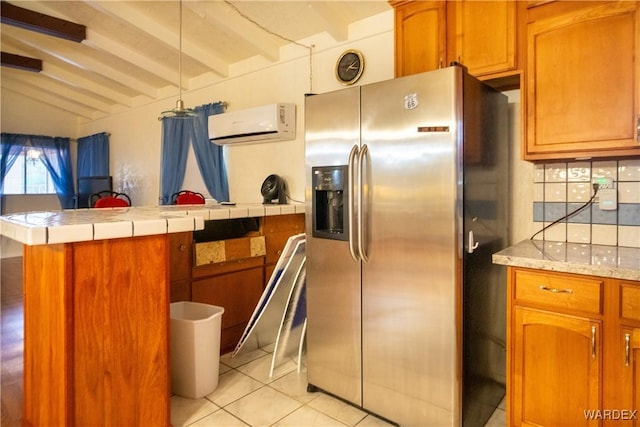 kitchen featuring beam ceiling, light countertops, a wall mounted AC, brown cabinetry, and stainless steel fridge with ice dispenser