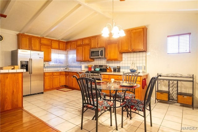 kitchen with brown cabinetry, appliances with stainless steel finishes, backsplash, hanging light fixtures, and a notable chandelier