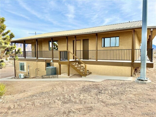 back of house featuring central air condition unit, metal roof, and stucco siding