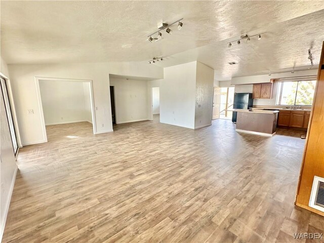 unfurnished living room featuring light wood-style floors, visible vents, a sink, and a textured ceiling