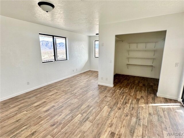 unfurnished bedroom featuring a spacious closet, a textured ceiling, baseboards, and wood finished floors