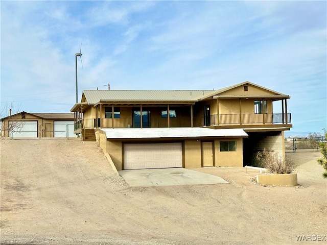 view of front of home with a balcony, a garage, dirt driveway, and stucco siding