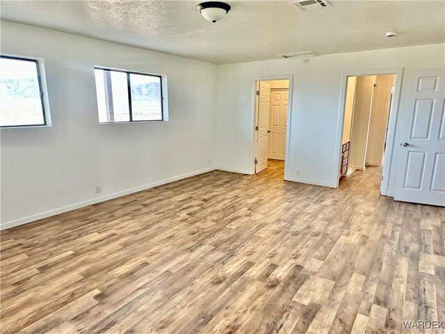 unfurnished bedroom featuring light wood-style floors, visible vents, baseboards, and a textured ceiling