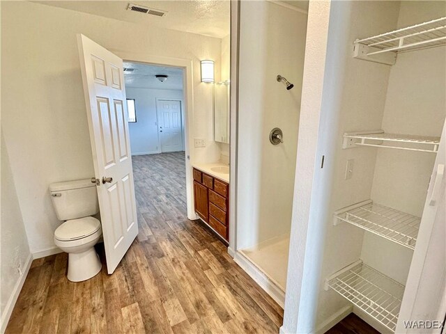 bathroom featuring toilet, wood finished floors, vanity, visible vents, and baseboards