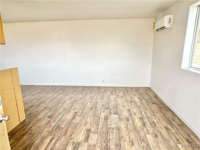 unfurnished room with wood finished floors, baseboards, and a wall mounted AC