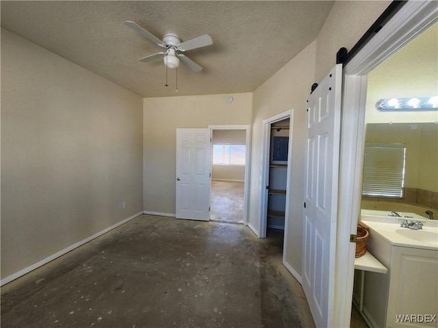 interior space with a barn door, unfinished concrete flooring, connected bathroom, baseboards, and a textured ceiling