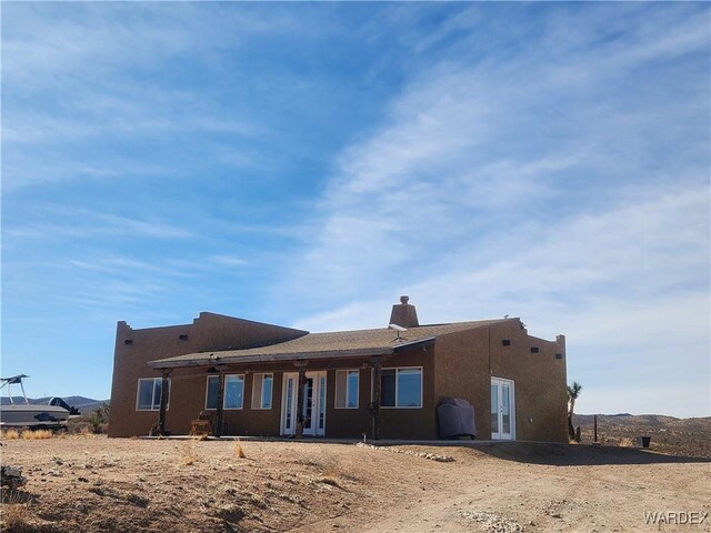 back of house featuring french doors, a chimney, and stucco siding