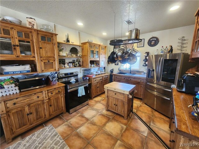 kitchen featuring visible vents, brown cabinetry, glass insert cabinets, appliances with stainless steel finishes, and light countertops