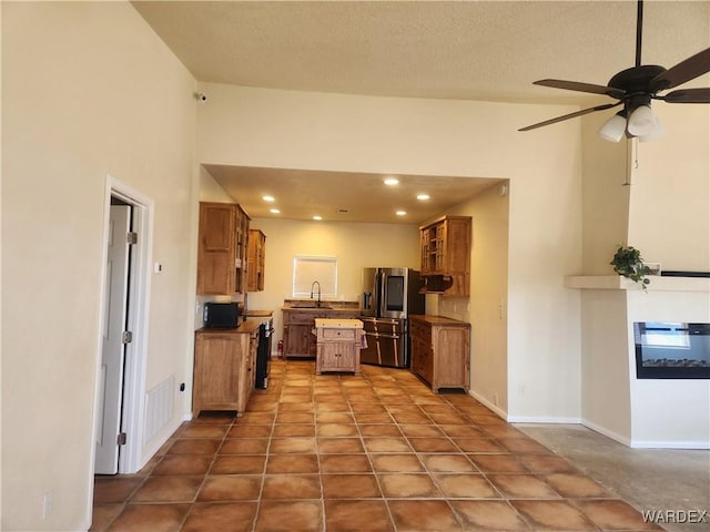 kitchen with a ceiling fan, a sink, stainless steel fridge, and brown cabinets