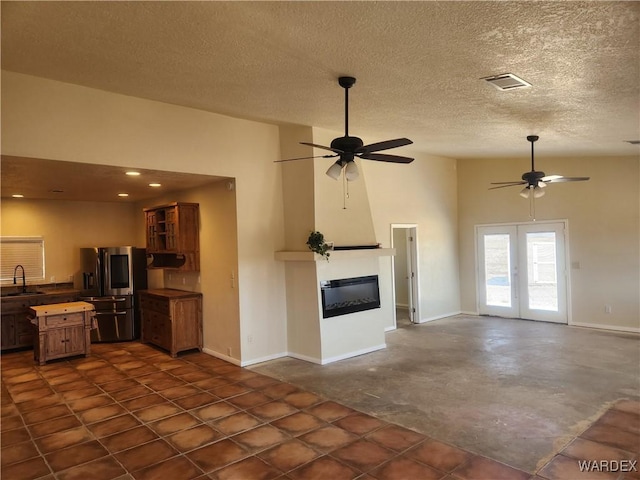 unfurnished living room with visible vents, a sink, baseboards, a glass covered fireplace, and ceiling fan