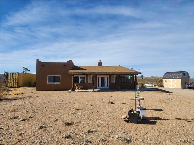 view of front of house with an outdoor structure, fence, french doors, stucco siding, and a shed