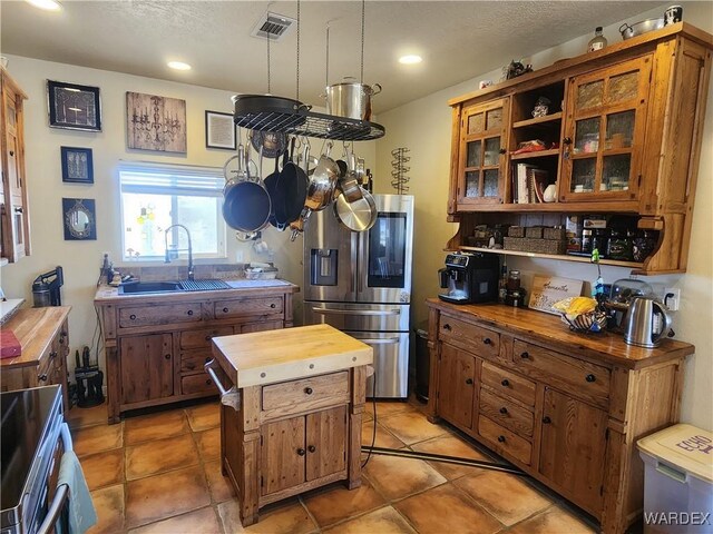 kitchen featuring stainless steel appliances, a sink, visible vents, wooden counters, and glass insert cabinets