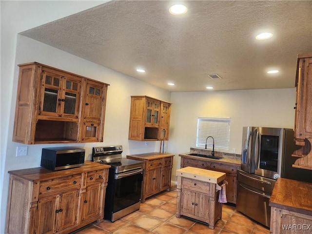 kitchen featuring stainless steel appliances, a sink, visible vents, butcher block counters, and brown cabinetry