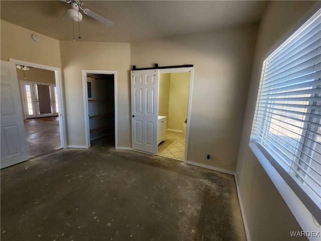 unfurnished bedroom with connected bathroom, a barn door, concrete floors, and baseboards