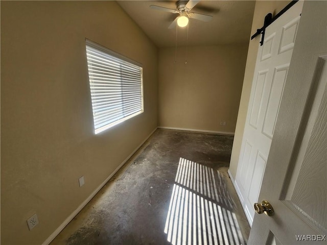 spare room with ceiling fan, baseboards, unfinished concrete floors, and a barn door