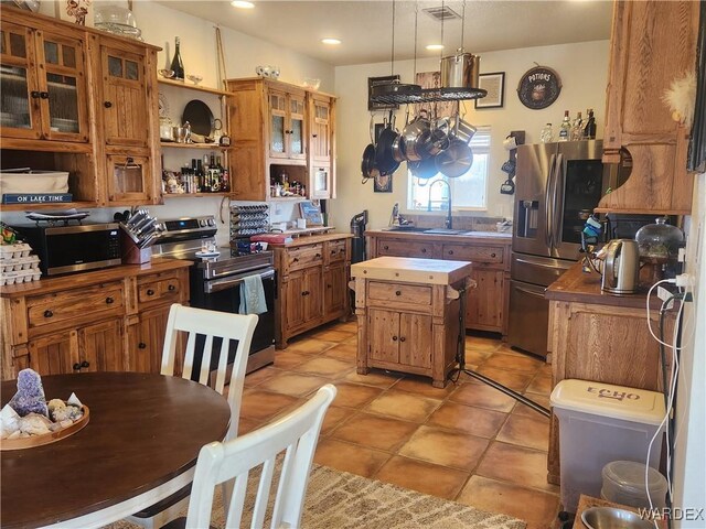 kitchen with brown cabinetry, a center island, stainless steel appliances, light countertops, and a sink