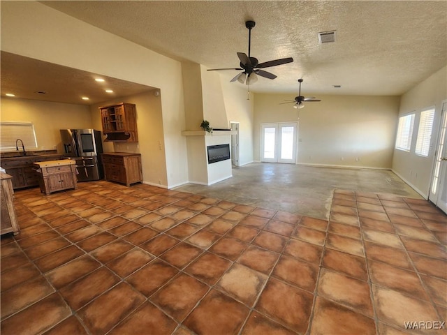 unfurnished living room featuring ceiling fan, a wealth of natural light, a sink, and visible vents