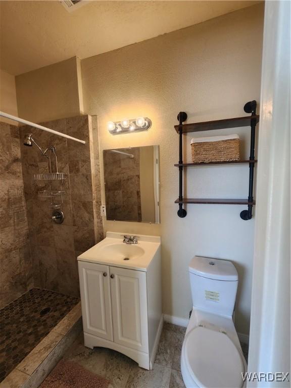 full bath with toilet, baseboards, vanity, and tiled shower