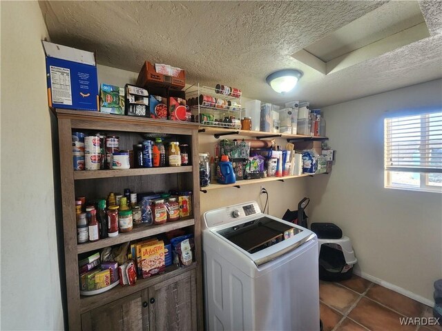 clothes washing area featuring washer / clothes dryer, a textured ceiling, laundry area, baseboards, and tile patterned floors