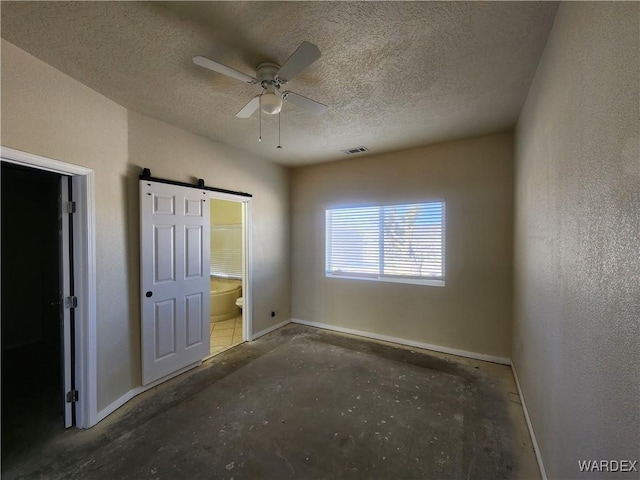 unfurnished bedroom with a barn door, a textured ceiling, ensuite bathroom, baseboards, and visible vents