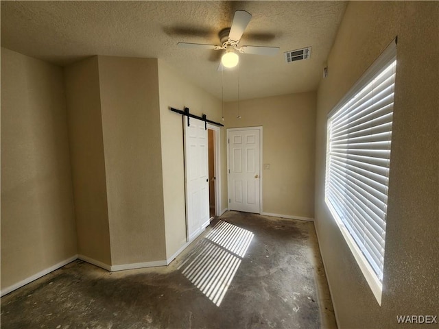 interior space with a barn door, a textured ceiling, visible vents, and baseboards