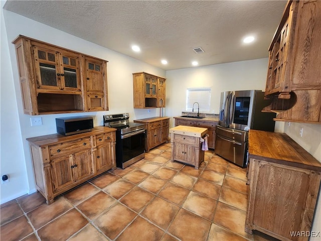 kitchen featuring stainless steel appliances, a sink, visible vents, butcher block countertops, and brown cabinetry