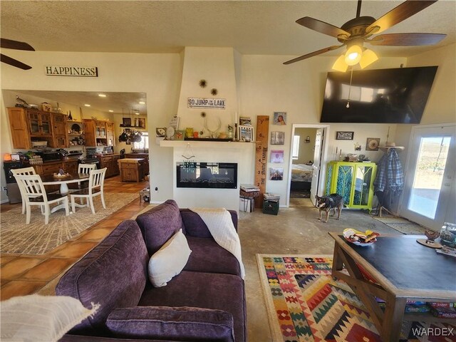 living room featuring ceiling fan, a textured ceiling, and a glass covered fireplace