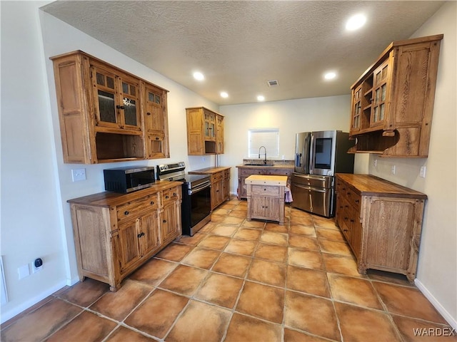 kitchen featuring brown cabinetry, a sink, appliances with stainless steel finishes, and a kitchen island