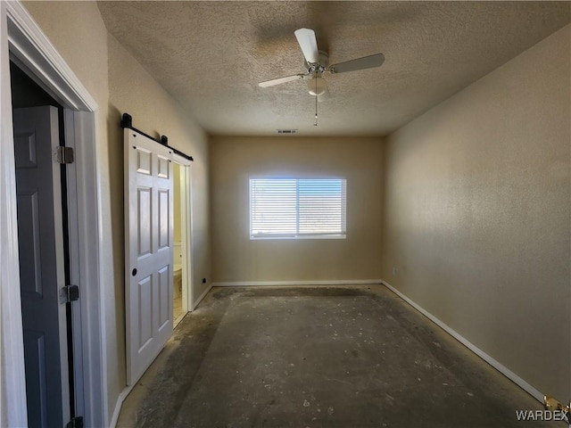 spare room featuring a textured ceiling, a barn door, visible vents, baseboards, and ceiling fan
