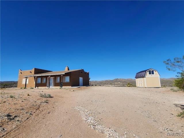 back of house featuring a storage shed, a mountain view, a chimney, an outdoor structure, and stucco siding