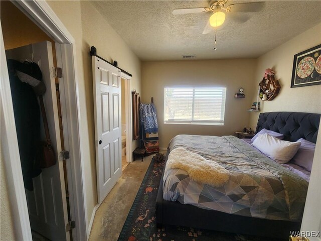 bedroom featuring a ceiling fan, a barn door, visible vents, and a textured ceiling