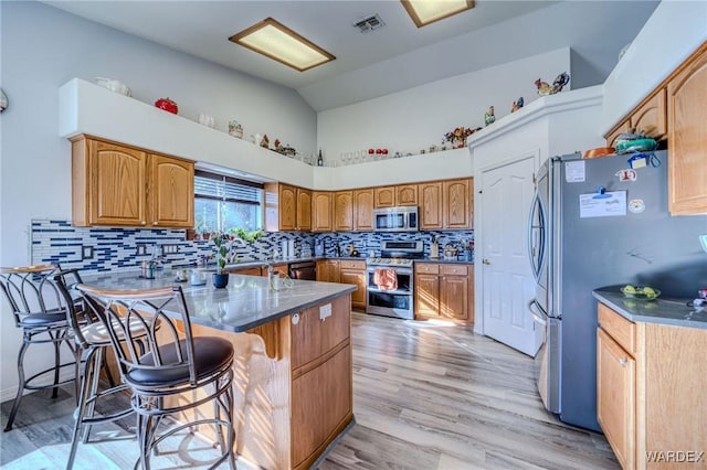 kitchen featuring stainless steel appliances, tasteful backsplash, brown cabinetry, a peninsula, and a kitchen breakfast bar