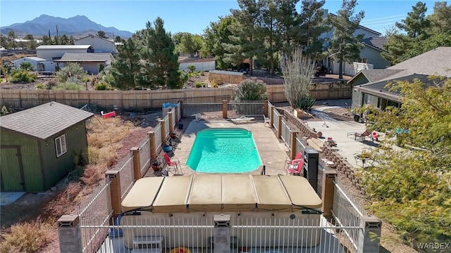 view of swimming pool with a fenced in pool, a fenced backyard, an outdoor structure, a shed, and a mountain view