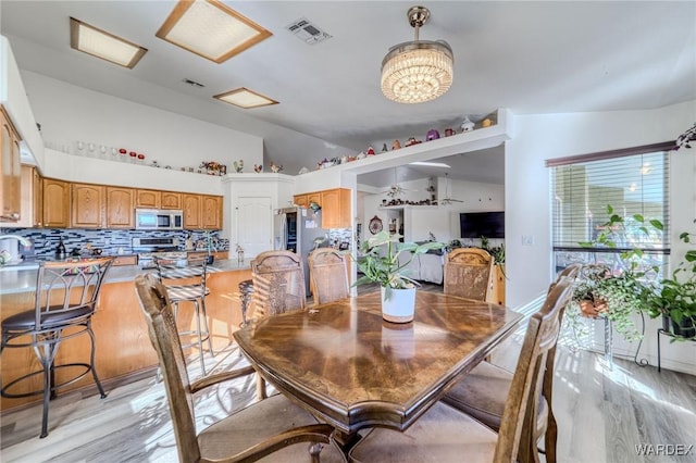 dining room featuring vaulted ceiling, visible vents, and light wood-style floors