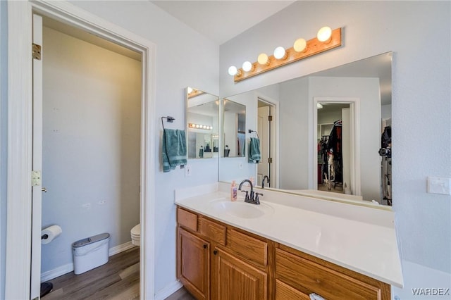 bathroom featuring toilet, wood finished floors, vanity, baseboards, and a walk in closet