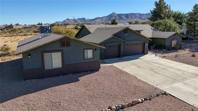 single story home with a garage, concrete driveway, a mountain view, and stucco siding