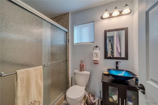 bathroom featuring a stall shower, a textured wall, vanity, and toilet