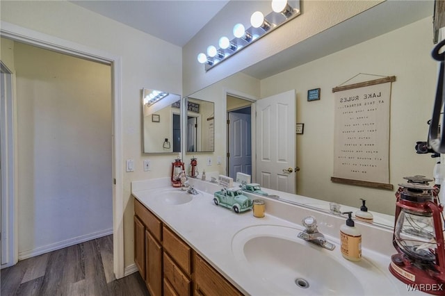 bathroom with wood finished floors, a sink, baseboards, and double vanity