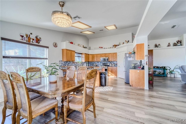 dining area featuring visible vents, light wood-style flooring, and an inviting chandelier