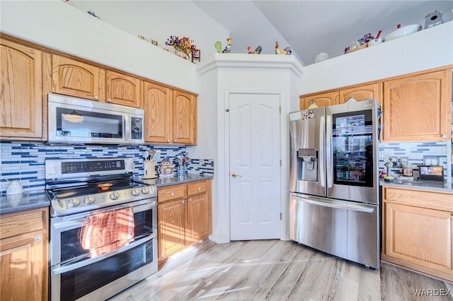 kitchen featuring dark countertops, lofted ceiling, stainless steel appliances, light wood-style floors, and backsplash