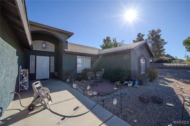 exterior space with a patio area, roof with shingles, and stucco siding