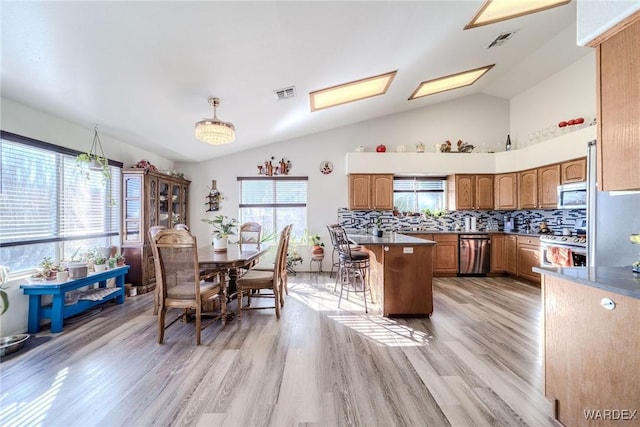 kitchen featuring appliances with stainless steel finishes, brown cabinetry, visible vents, and a kitchen breakfast bar